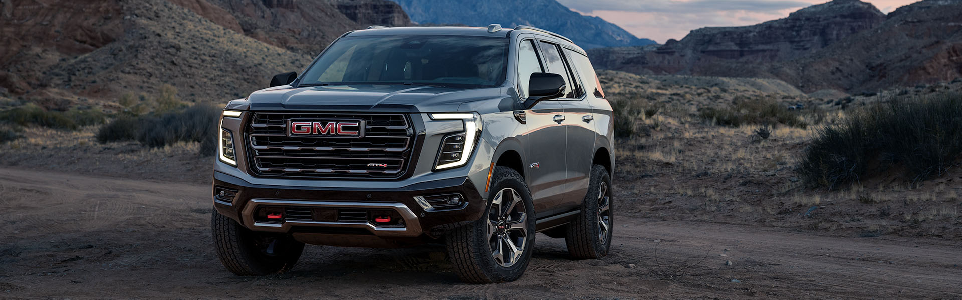 A 2026 GMC Yukon AT4 parked on a dirt road with rocky hills in the background.